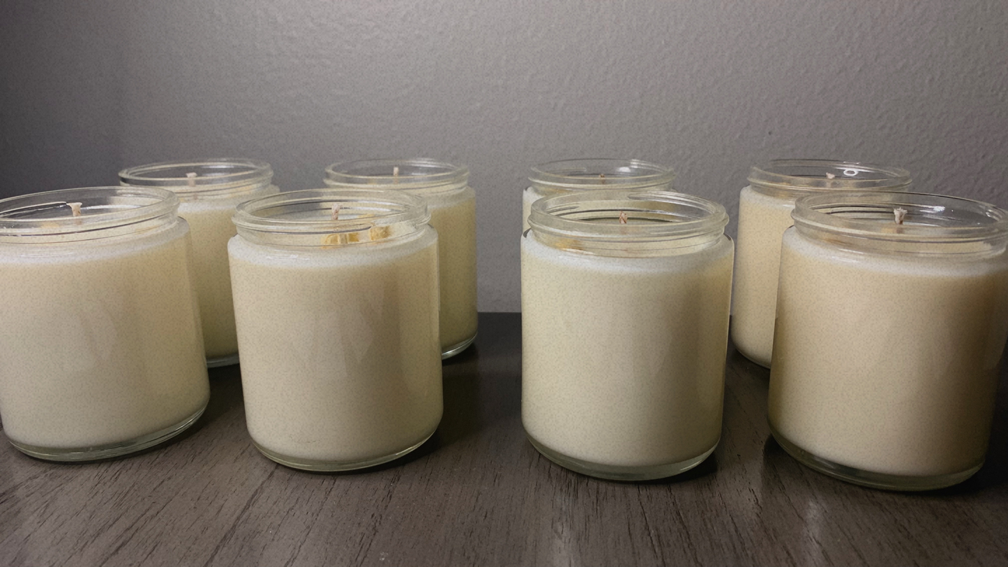 Row of white candles in glass jars on a wooden surface with a gray wall background